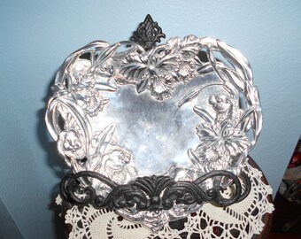 May include: A silver serving dish with an ornate design of flowers and leaves. The dish is on a black metal stand.