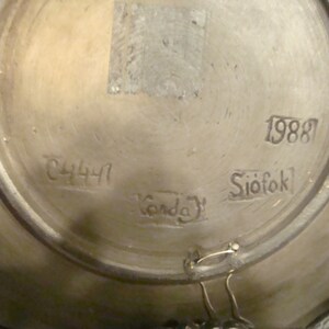 May include: Close-up of the bottom of a ceramic plate with the numbers 1988 and 2441, the word "Siofok" and the word "Garda" written on it.