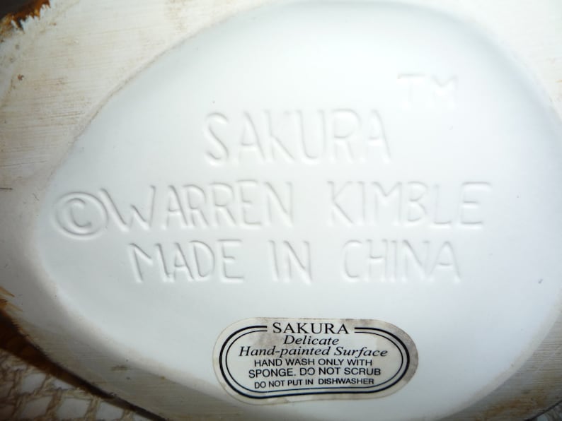 Peut inclure: Figurines en c&eacute;ramique blanche avec les mots "SAKURA WARREN KIMBLE MADE IN CHINA" au bas. Un autocollant sur la figurine indique "SAKURA Delicate Hand-painted Surface HAND WASH ONLY WITH SPONGE. DO NOT SCRUB DO NOT PUT IN DISHWASHER."