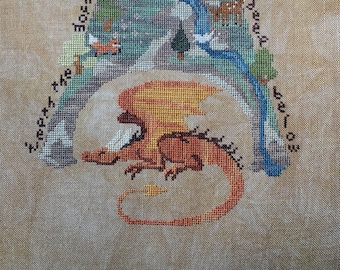 May include: Cross-stitch embroidery depicting a mountain scene with a dragon underneath. The mountain is white with a blue river flowing down it. The text reads "Where the red snow is capped, a dragon in the Elder sleeps below".