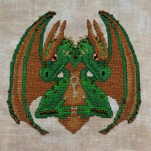 May include: Cross-stitch embroidery of two green dragons with brown wings and gold accents. The dragons are facing each other with their heads touching.