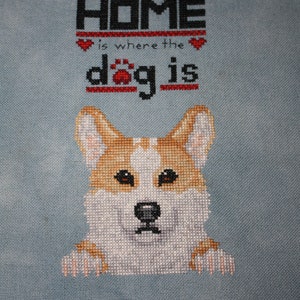 Può includere: Ricamo a punto croce di un cane corgi che spunta da dietro un cartello con la scritta "Home is where the dog is".