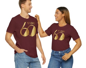 May include: Two people wearing maroon t-shirts with a gold "Studio 60" graphic design. The shirts are a casual style with short sleeves.