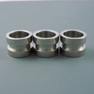 May include: Three silver metal rings with a slightly wider top and bottom. The rings are smooth and shiny.