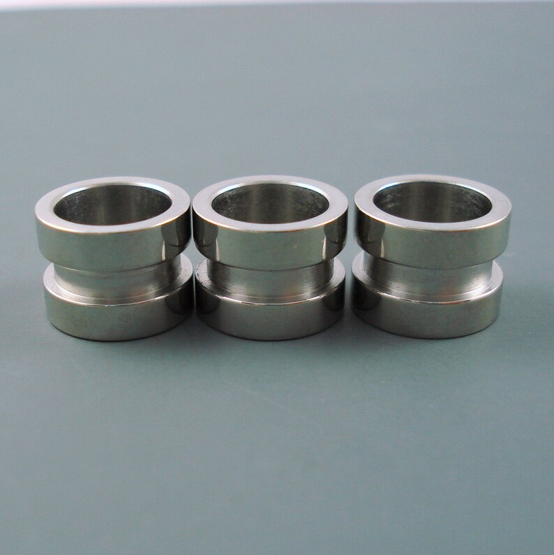 May include: Three silver metal rings with a slightly wider top and bottom. The rings are smooth and shiny.