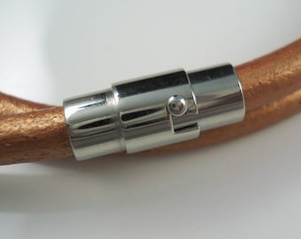 May include: A close-up of a brown leather bracelet with a silver magnetic clasp. The clasp has a small, round button on the side.