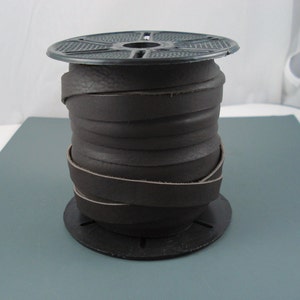 May include: A spool of brown leather cord wrapped around a black plastic spool. The cord is approximately 1/2 inch wide.