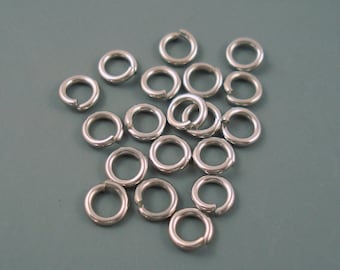 May include: A collection of small, silver-colored jump rings scattered on a gray surface. Each ring is circular with a small opening, ready to be connected. These jewelry findings are ideal for crafting and jewelry making.