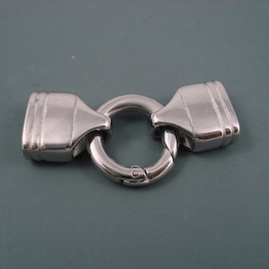 May include: A silver metal clasp with a round ring and two rectangular pieces on either side. The clasp is designed to connect two pieces of jewelry or other items.
