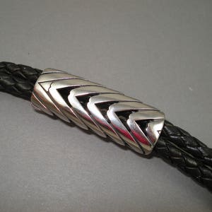 May include: A silver bolo tie with a braided black leather cord and a geometric patterned silver slider.