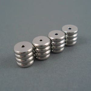 May include: Four silver metal beads with a hole in the center. Each bead is made of multiple stacked rings.