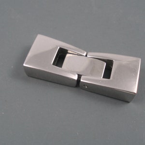 May include: A silver-toned metal clasp for a necklace or bracelet. The clasp is made of two pieces that fit together to secure the jewelry.