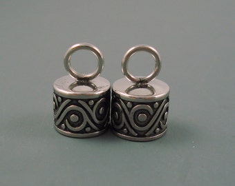 May include: Two silver metal cord ends with a decorative swirl pattern and a loop at the top.