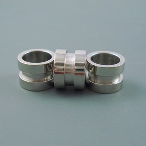May include: Three silver metal rings, each with a smooth, rounded surface. The rings are stacked together, creating a decorative design.