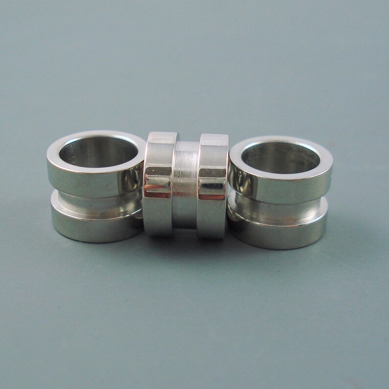 May include: Three silver metal rings, each with a smooth, rounded surface. The rings are stacked together, creating a decorative design.