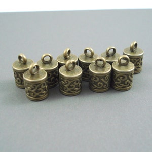 May include: Ten antique gold-toned metal cord ends with a decorative swirl design. Each end has a small loop for attaching to a cord or string.