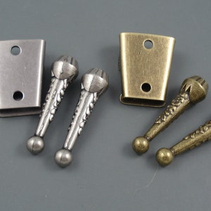 May include: Two sets of decorative metal hardware for furniture. Each set includes two ornate metal pulls and a rectangular metal plate with two holes. One set is silver and the other is gold.