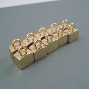 May include: Ten gold-colored metal clasps with a loop on top. The clasps are arranged in a row, with the loops facing the viewer.