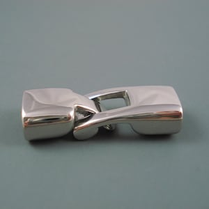 May include: A silver-toned metal clasp for a bracelet or necklace. The clasp is made of two pieces that fit together securely.