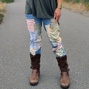 May include: A dark olive green short-sleeved t-shirt paired with blue denim jeans featuring various fabric patches in floral, striped, and solid patterns. The outfit is completed with brown leather mid-calf boots and a wide gold-toned metal cuff bracelet.