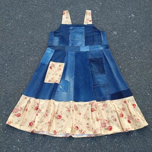 May include: A sleeveless pinafore dress constructed from various shades of blue denim patches and cream-colored fabric featuring a red and pink floral pattern. The bodice includes a denim pocket, while the skirt features a pleated floral hem.