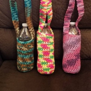 May include: Three crocheted water bottle holders with different color patterns. The holders are made with a variety of colors, including teal, brown, pink, green, yellow, and white.