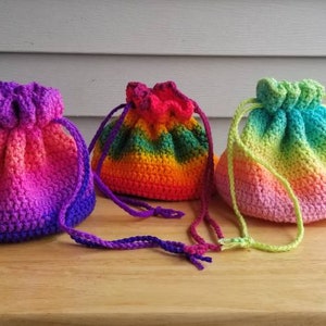 Könnte beinhalten: Drei gehäkelte Beutel mit Kordelzug in Regenbogen-Ombre-Farben. Die Beutel sind aus verschiedenen Farben gefertigt, darunter Rosa, Orange, Gelb, Grün, Blau und Lila. Die Beutel haben alle unterschiedliche Größen und Kordelzuglängen.