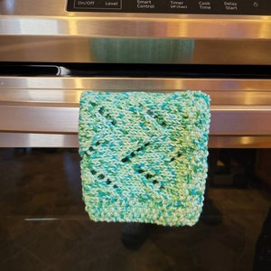 May include: A green and blue knitted dishcloth hangs on the handle of a stainless steel oven. The oven has a digital display showing the time 9:08.