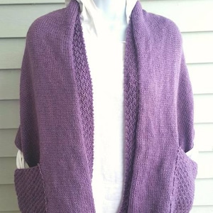 May include: A purple knitted cardigan with pockets and a shawl collar.