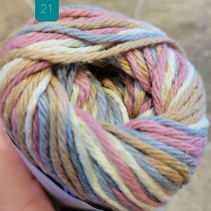 May include: A ball of yarn with a multi-colored striped pattern in shades of pink, beige, white, and blue. The yarn is labeled with the number "21".