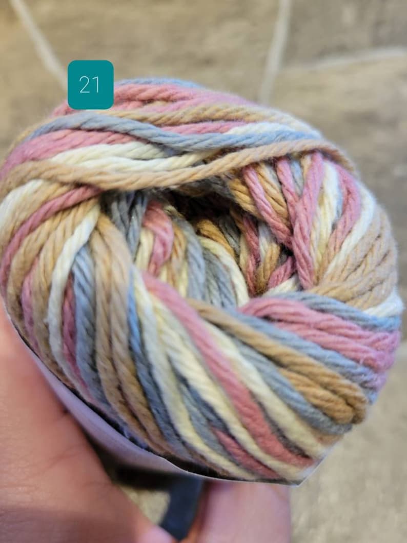 May include: A ball of yarn with a multi-colored striped pattern in shades of pink, beige, white, and blue. The yarn is labeled with the number "21".
