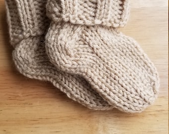May include: A pair of beige knitted socks with a folded cuff. The socks are made from a soft, warm yarn and have a simple, classic design.