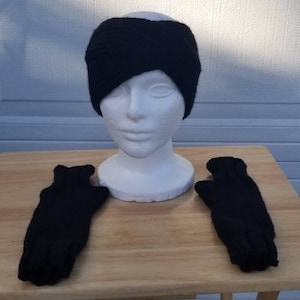 May include: A black knit headband and a pair of black fingerless gloves. The headband is folded over and the gloves are laying flat on a wooden table.