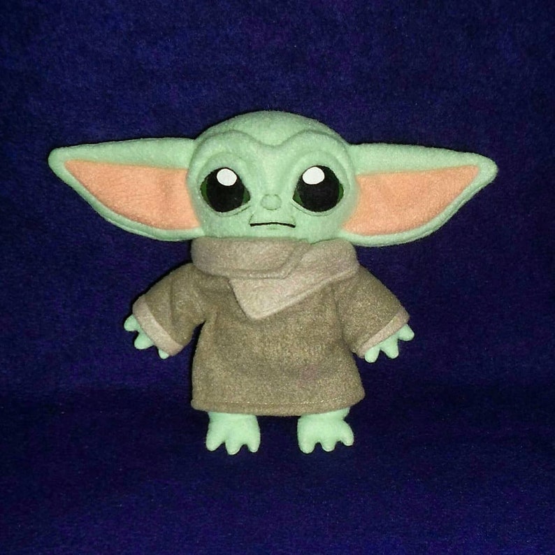 May include: A green plush toy with large eyes and a brown robe. The toy is a popular character from the Star Wars franchise.
