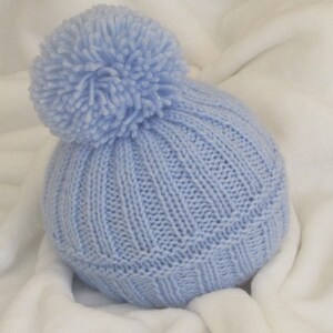 May include: A light blue knitted baby hat with a fluffy pom-pom on top.