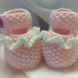 Può includere: Un paio di scarpine per neonati in crochet rosa con bordo in pizzo bianco e bottoni rosa.