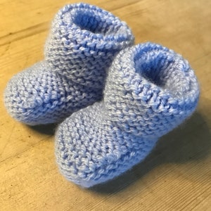 May include: A pair of light blue knitted baby booties. The booties are made with a soft, textured yarn and have a simple, classic design.