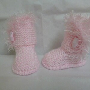 May include: A pair of pink knitted baby booties with fluffy white trim and a pink button on each bootie.
