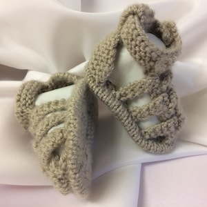 Puede incluir: Un par de botitas de bebé de punto beige con un diseño de correa cruzada.
