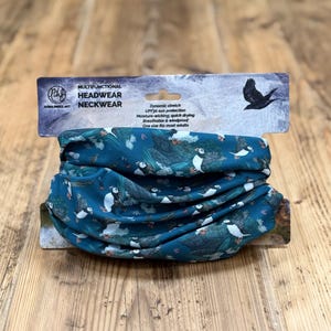 May include: Teal multifunctional headwear and neckwear featuring a pattern of white and black birds. The packaging states it offers dynamic stretch, UPF30 sun protection, moisture-wicking, quick drying, breathability, and windproof qualities. One size fits most adults.