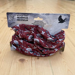 Peut inclure: Un tour de cou multifonctionnel bordeaux orné d'un motif répétitif d'oiseaux noirs et blancs, de rochers gris et de feuillage vert. L'emballage porte le texte MULTIFUNCTIONAL HEADWEAR NECKWEAR, RONA INNES ART et mentionne une protection solaire UPF30.