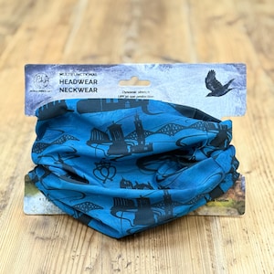 Puede incluir: Un pañuelo multifuncional azul para la cabeza y el cuello con un diseño de paisaje urbano negro. La tela tiene elasticidad dinámica y protección solar UPF 30. El embalaje dice "Headwear Neckwear". Un pájaro vuela en la esquina superior derecha.