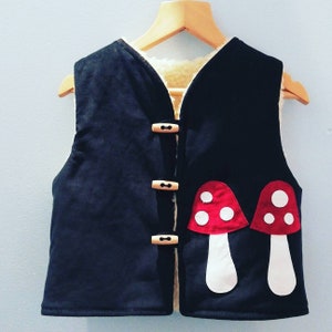 May include: A black corduroy waistcoat with a white sherpa lining and two red and white mushroom appliques. The waistcoat has wooden button fastenings.