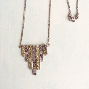May include: A gold and silver necklace with a geometric pendant made of multiple rectangular pieces. The pendant is textured and has a layered look.