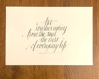 May include: A black and white calligraphy quote on a cream background. The quote reads "Art washes away from the soul the dust of everyday life."  The quote is attributed to Pablo Picasso.