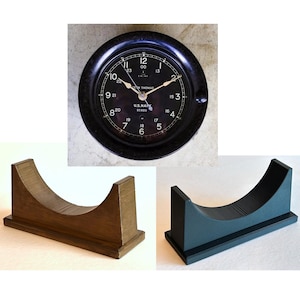 May include: A black clock with white numbers and hands, a white face with the text "U.S. NAVY 91020" and "BETH THOMAS INC."  The clock is on a wooden stand.