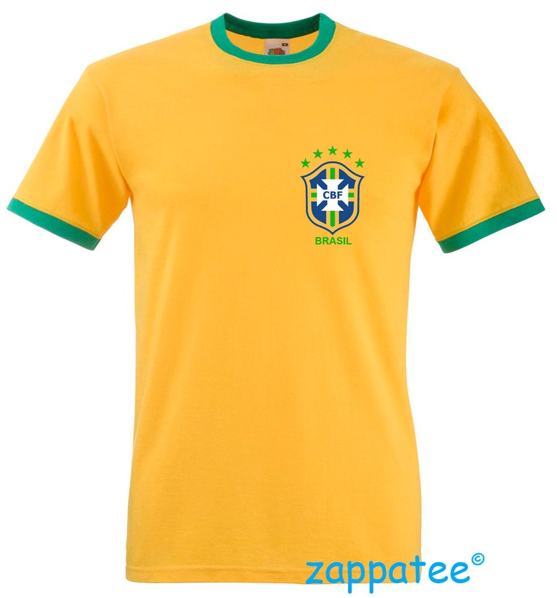 Pode incluir: Uma camiseta amarela com acabamentos verdes na gola e mangas. A camiseta apresenta o logotipo da Confedera&ccedil;&atilde;o Brasileira de Futebol (CBF) no peito esquerdo, com a palavra "BRASIL" abaixo. A camiseta &eacute; feita de um material macio.