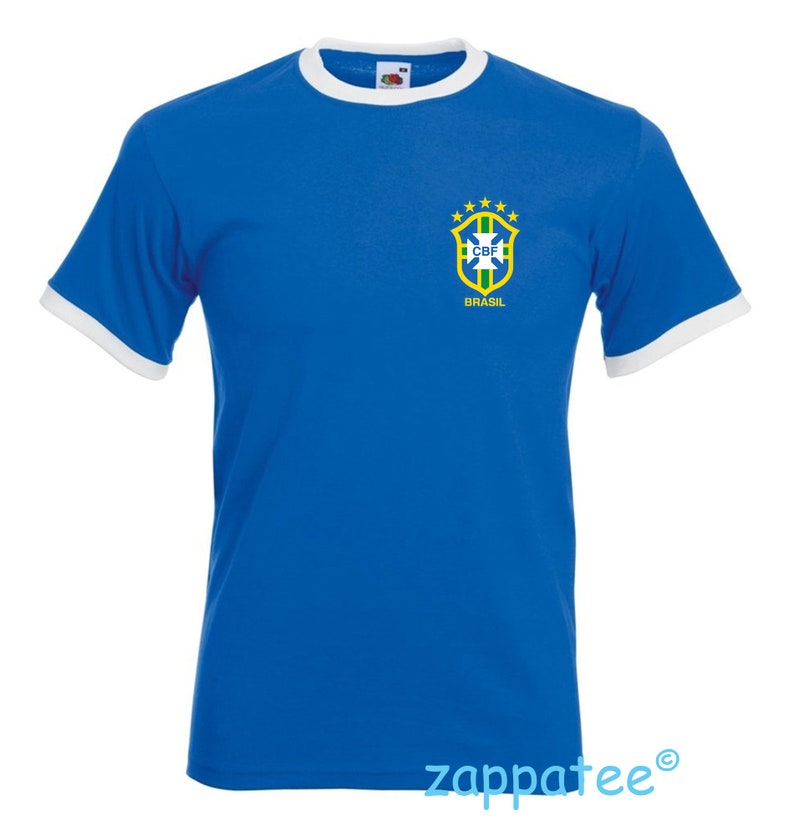 Pode incluir: Camiseta azul royal com acabamentos brancos na gola e mangas. A camisa apresenta o emblema da bandeira brasileira no peito esquerdo. O emblema inclui um escudo, estrelas e o texto "BRASIL".