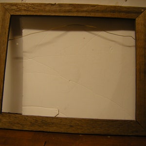 May include: A simple wooden picture frame with a wire hanger on the back. The frame is made of natural wood with a rustic finish.