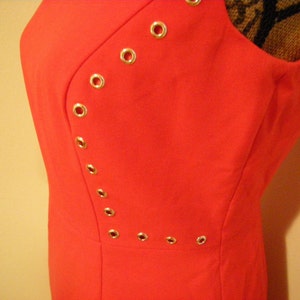 May include: A bright red sleeveless dress with a diagonal row of gold eyelets.